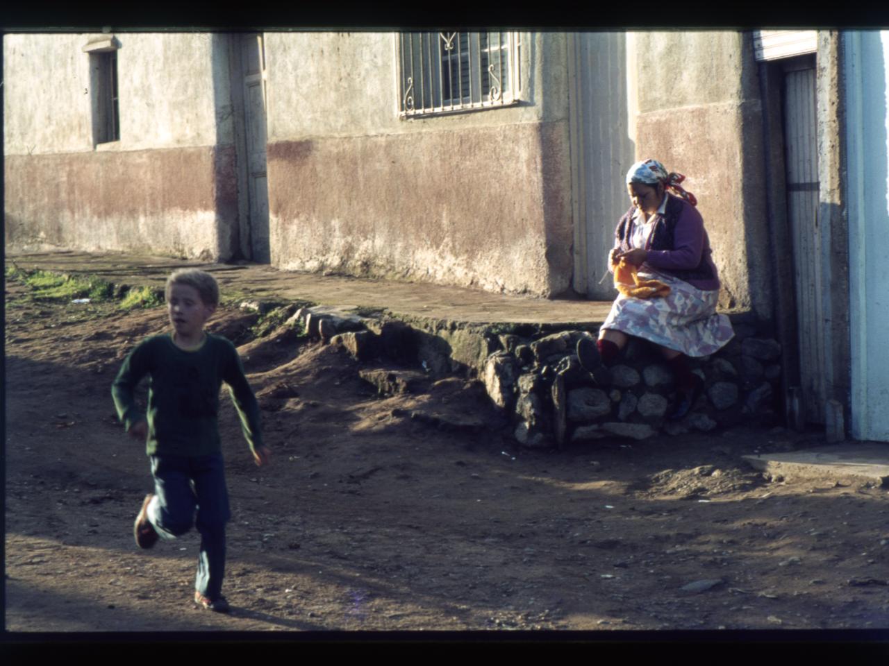 Mujer que teje delante de su casa con niño que corre , Cerro Cordillera