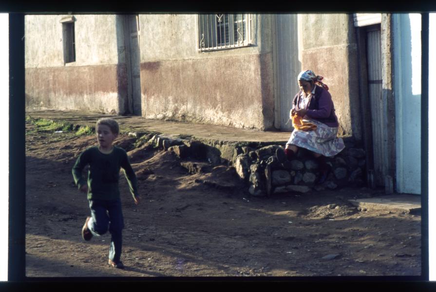 Mujer que teje delante de su casa con niño que corre , Cerro Cordillera